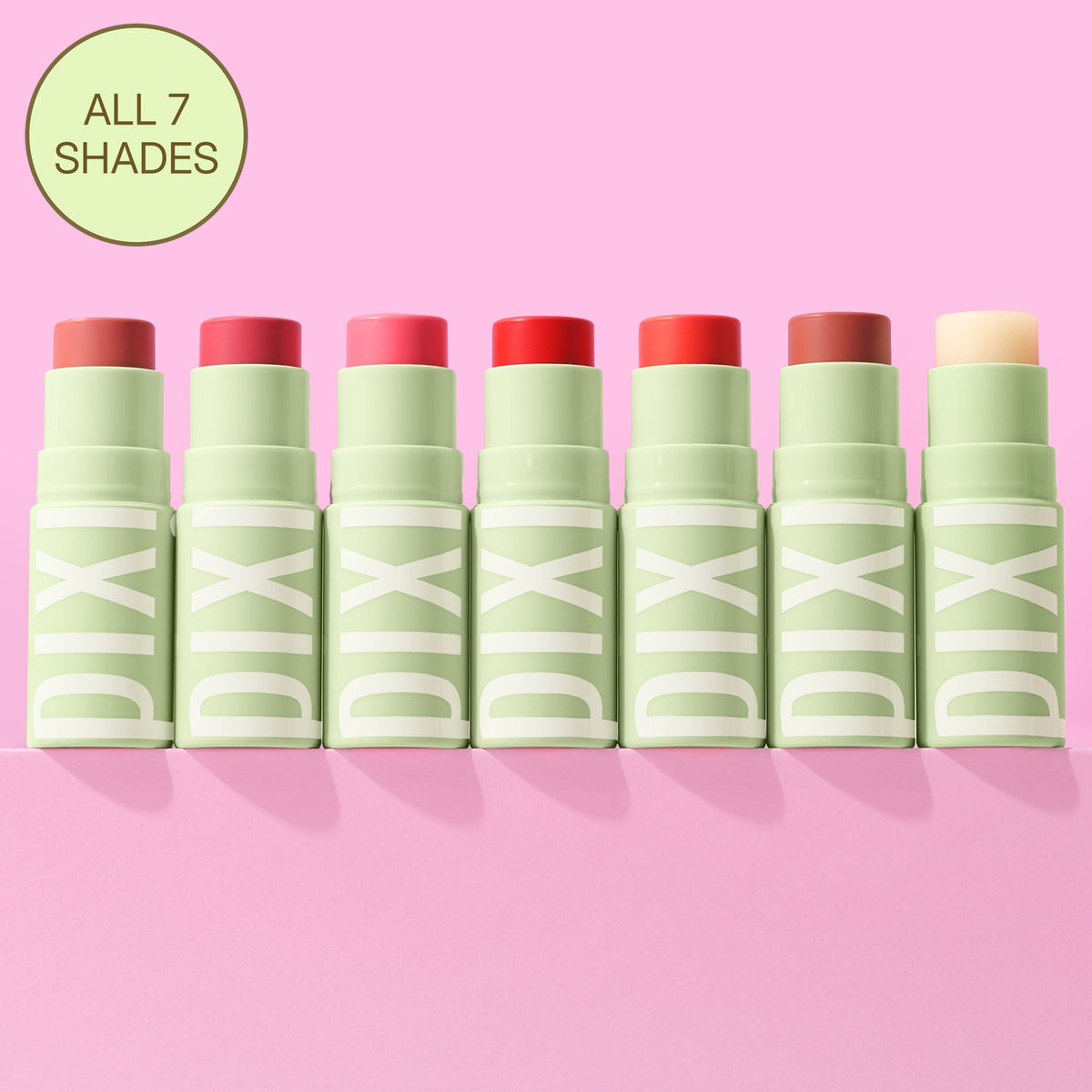 Seven PIXI lip balm tubes in different shades are lined up on a pink background, with a green circular badge in the top left that reads 'ALL 7 SHADES'.