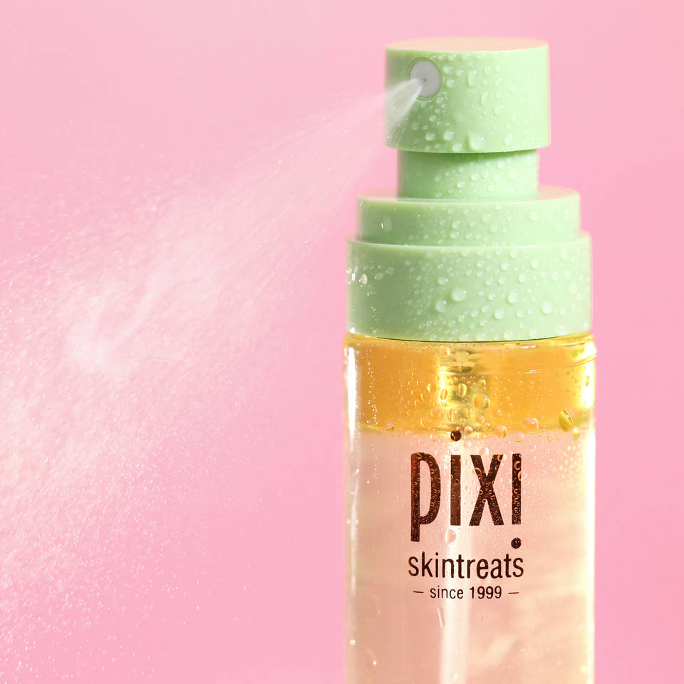 Pixi Skintreats facial mist bottle with a light green pump dispenser spraying a fine mist, set against a solid pink background. view 2
