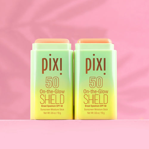 Two green PIXI sunscreen sticks on a pink background view 1